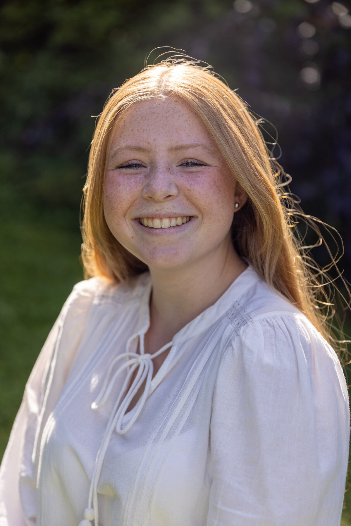 Portrettbilde av en ung jente som smiler mot kamera. Langt lyst hår, hvit bluse.