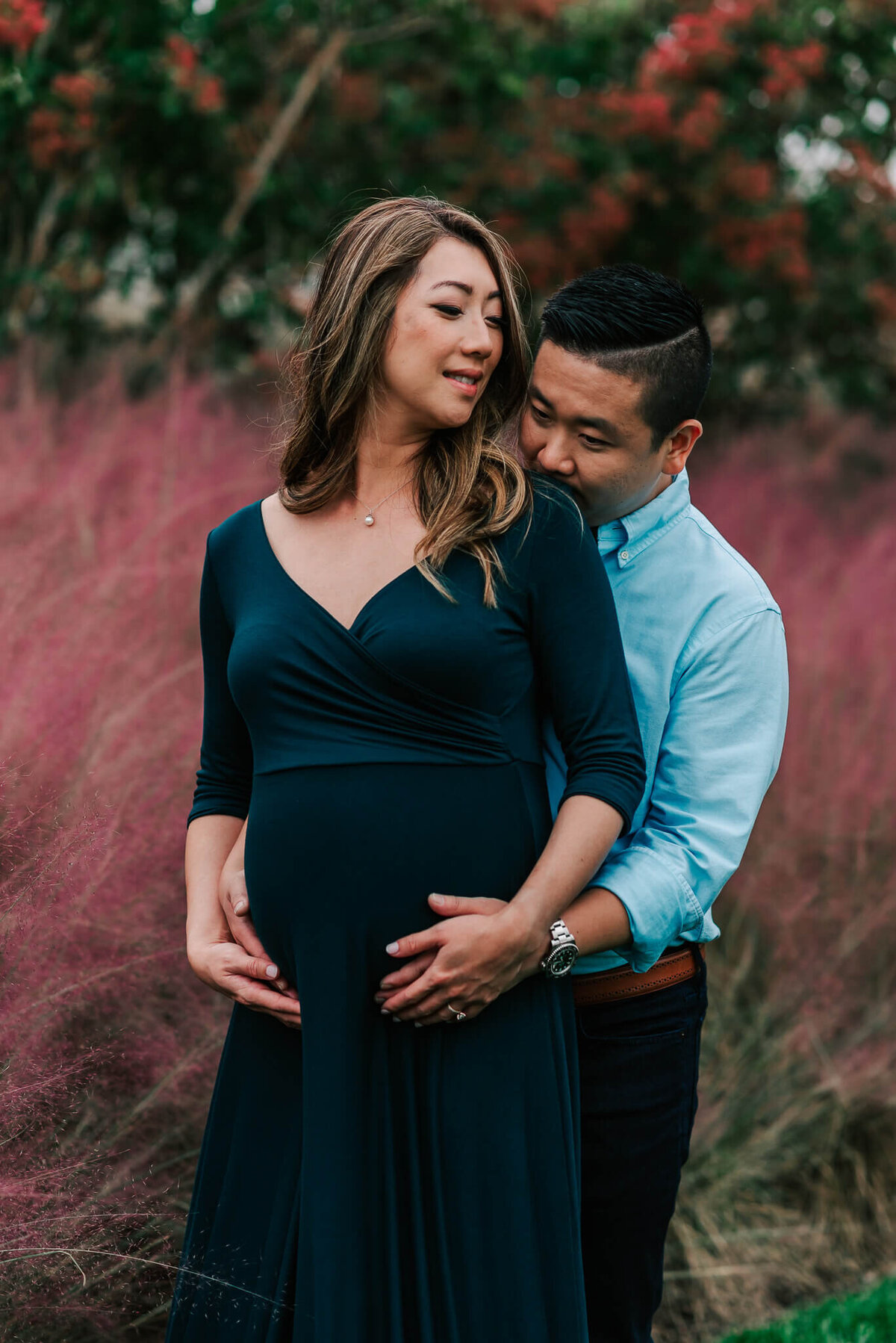 A pregnant woman smiles at her husband kissing her shoulder from behind