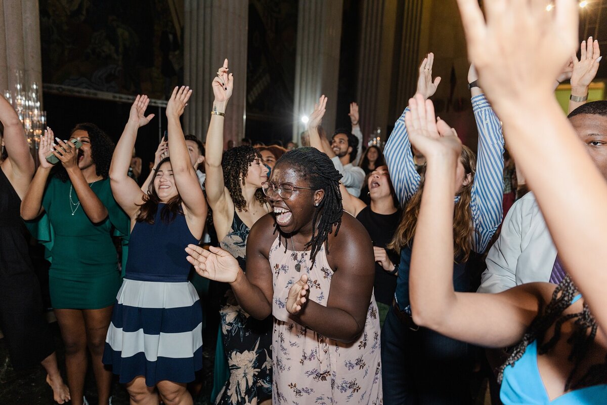Photo of a sea of wedding guests all celebrating and cheering with raised arms during a wedding reception at the Hall of State in Fair Park in Dallas, Texas.