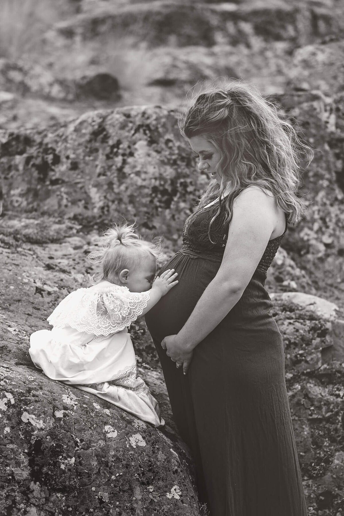 Black and white portrait of a little girl kissing her pregnant moms belly. Taken by Brittany Danielle Photography in Kamloops BC