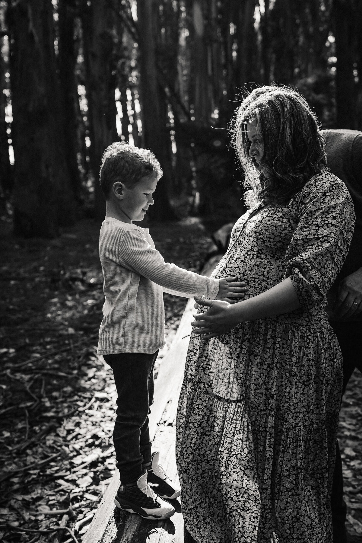 San Francisco boy touches mom's pregnant bellw with both hands.  Black and white backlit  photo