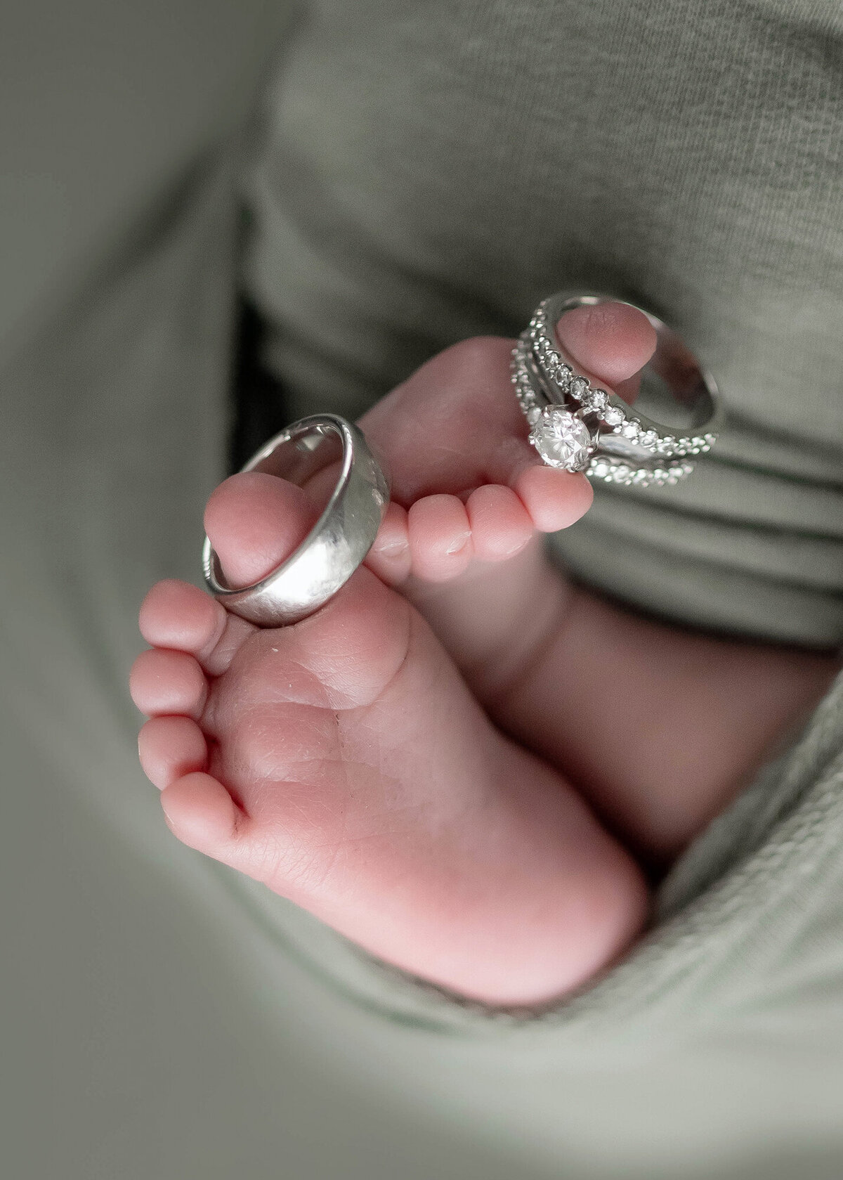 Wedding Rings hang on the toes of a newborn baby