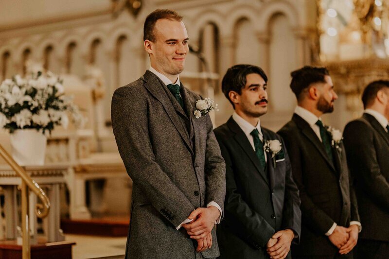 Le marié avec sur sa gauche les amis attendant à l'église la mariée, mains croisées. Immortalisé par Laura Termeau Photographie.