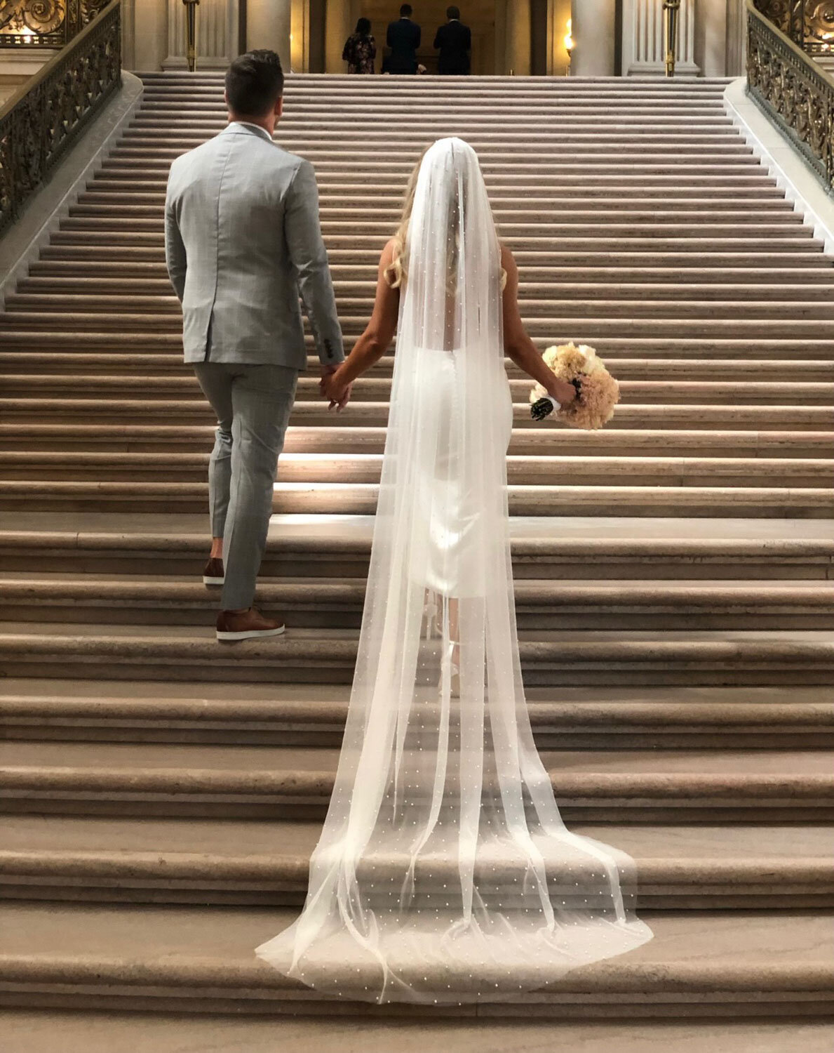 Bride and groom holding hands while walking up grand stairs