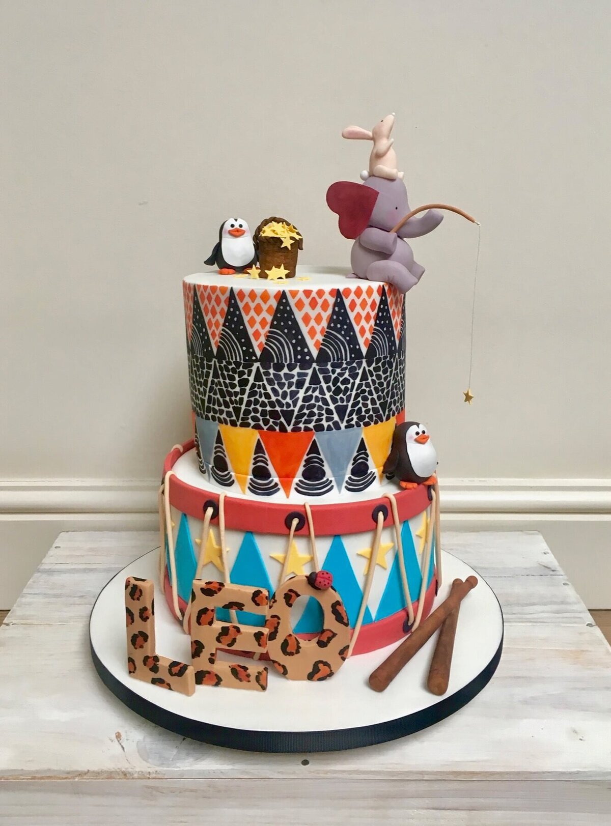 A funky birthday cake with two tiers and an elephant and mouse fishing along with 2 penguins