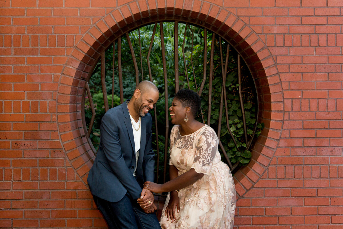 A couple holding hands and sitting in a small archway in a brick wall.