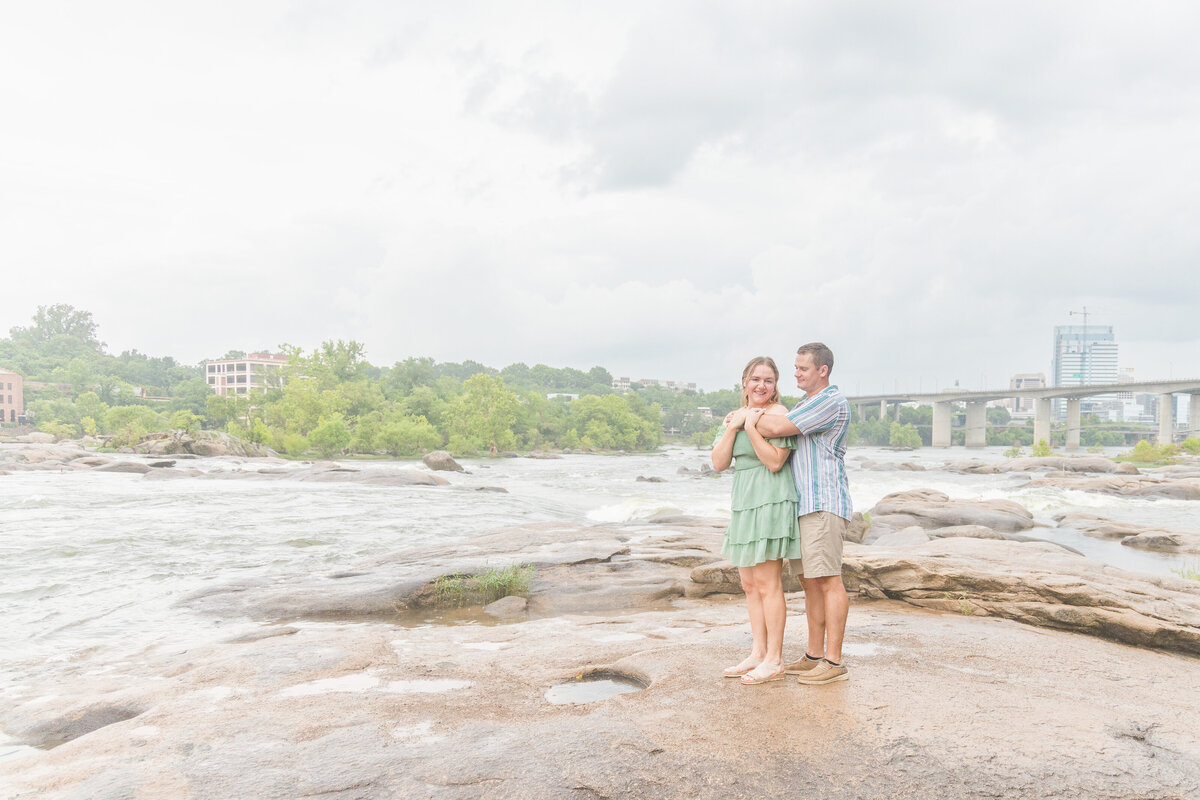 young man and woman standing on rocks beside James River holding each other