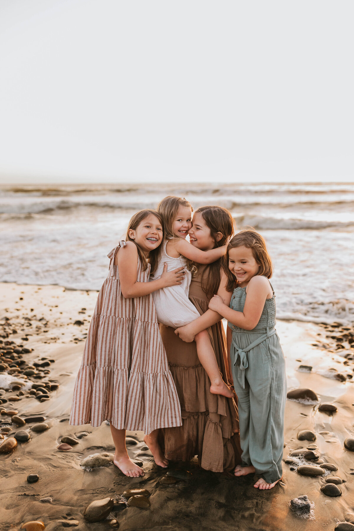 four young sisters hugging on the beach at golden hour