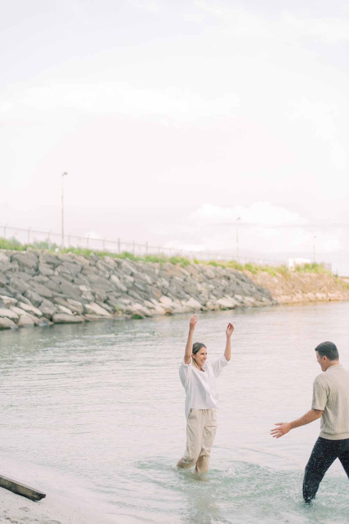 Couple laughing and dancing in the water, carefree and in love, against the calm Oakville lake.