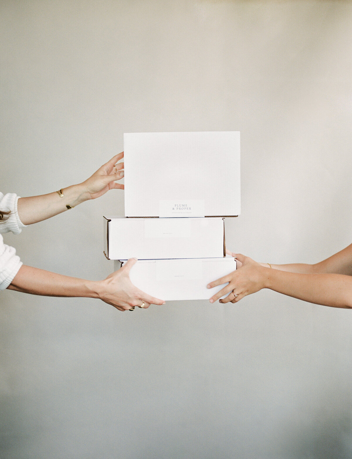 light beige backdrop, woman hands white branded boxes to friend, film brand photoshoot