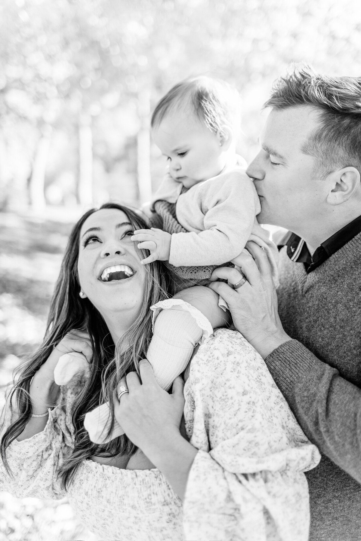 Black and white photo of parents laughing while holding their baby girl during her Kansas City first birthday milestone session.