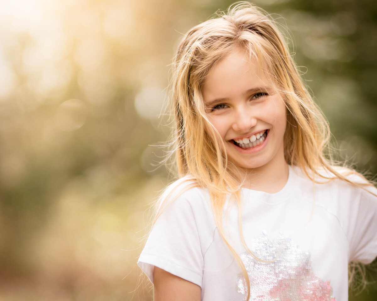 Young, blonde girl against golden lighting smiling in her portrait session