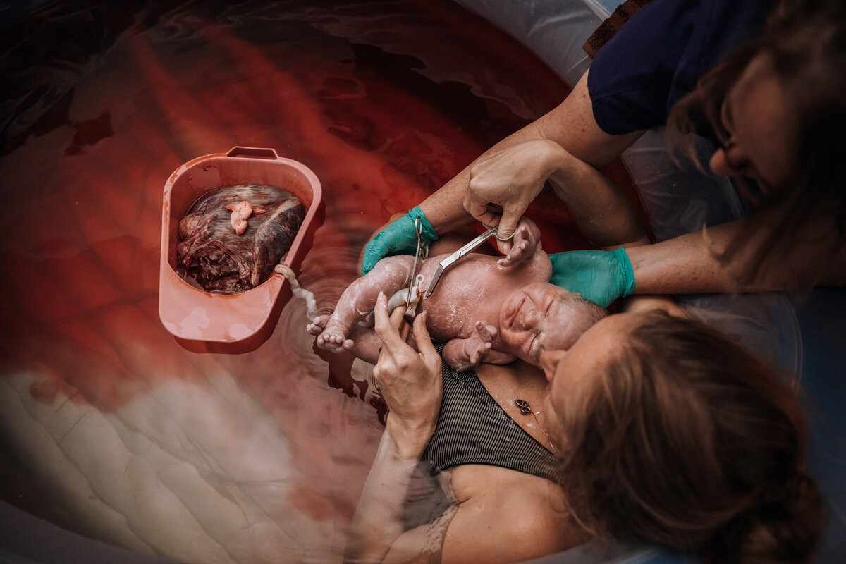woman in birth pool with newborn cutting umbilical cord
