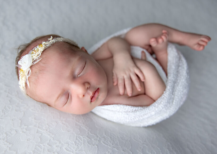 baby girl posed bum up on a white wooden bed in front of white backlit curtains.