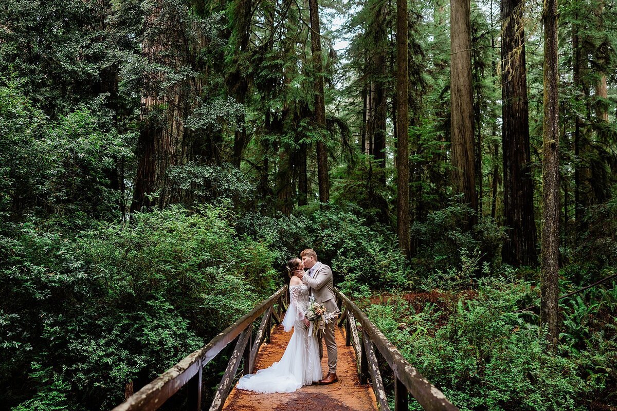 The eloping bride and groom embrace on a wooden bride in the California Redwoods.