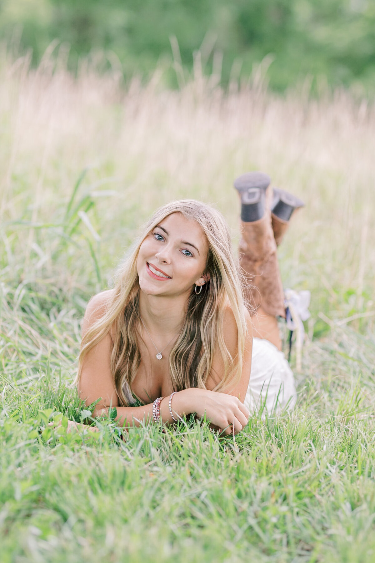 A high school senior laying in tall grass, smiling softly during her golden-hour field session — Raleigh portrait photographer.