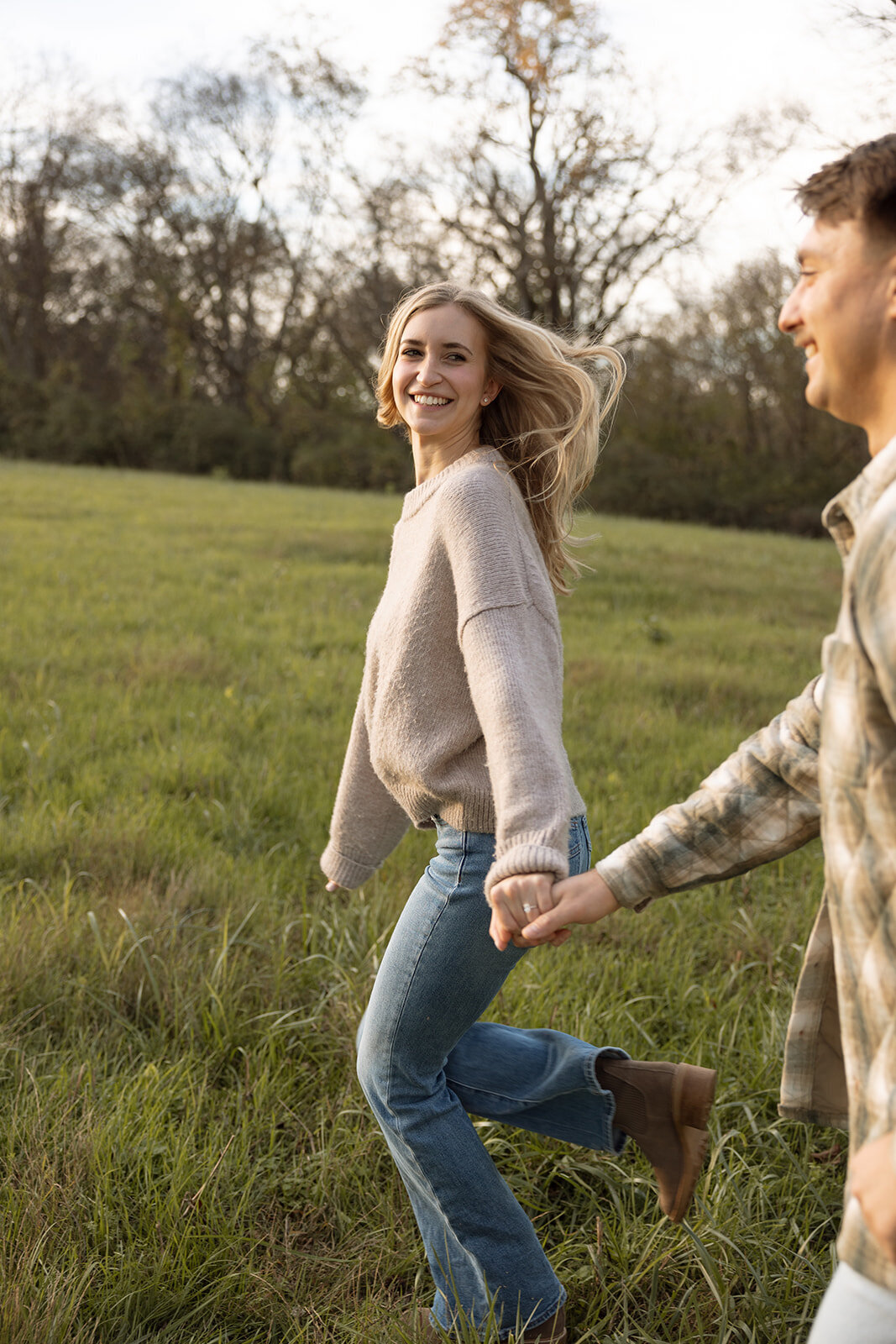Couple looks at each other as wind blows though her hair while walking hand in hand.