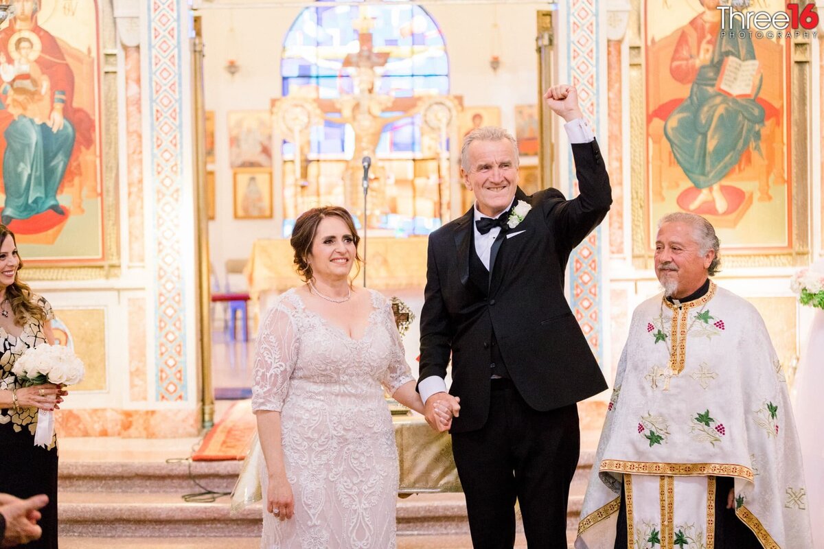 Groom lifts his hand in celebration as he and his Bride face their wedding guests