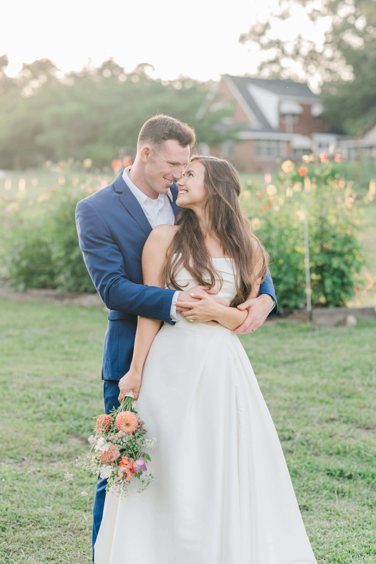 Alabama couple standing in a  field of greenery while groom wrpas his arm around the bride and bride is leaning her head on his shoulder