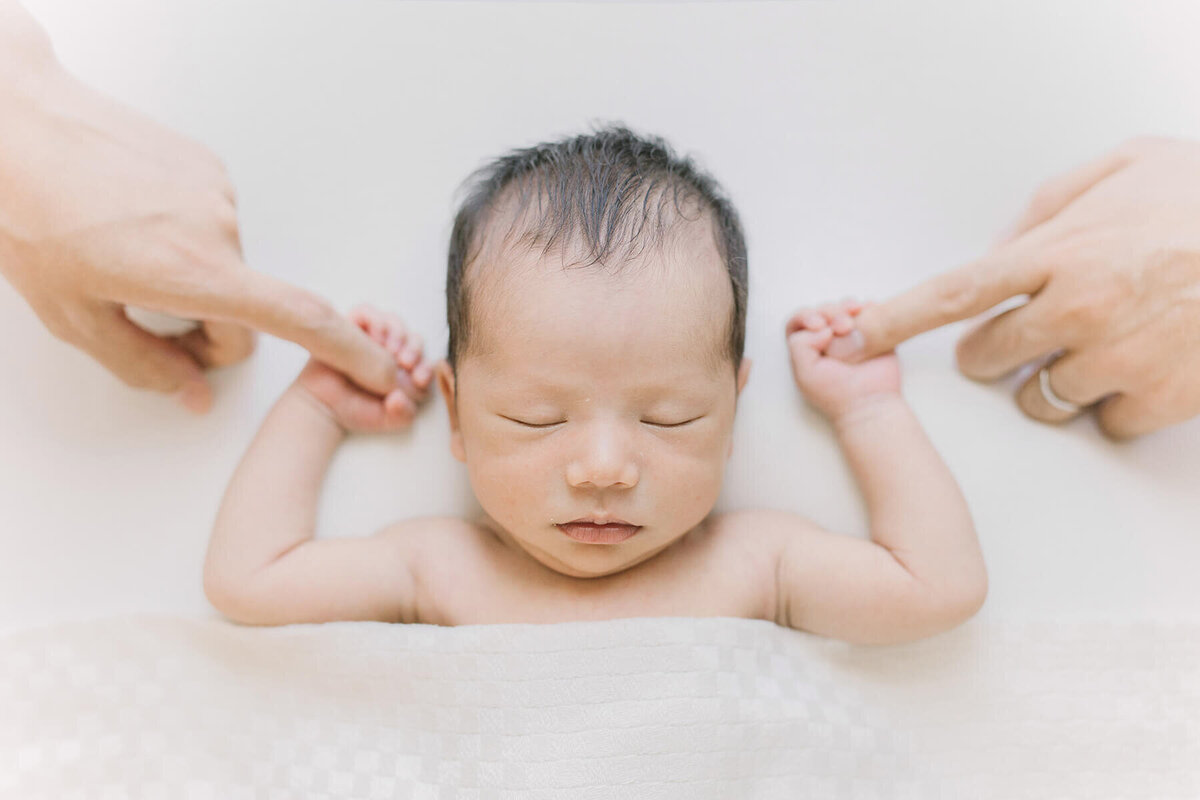 Newborn baby is sleeping on his back and holding fingers of his mother and father. Shot in Yokohama