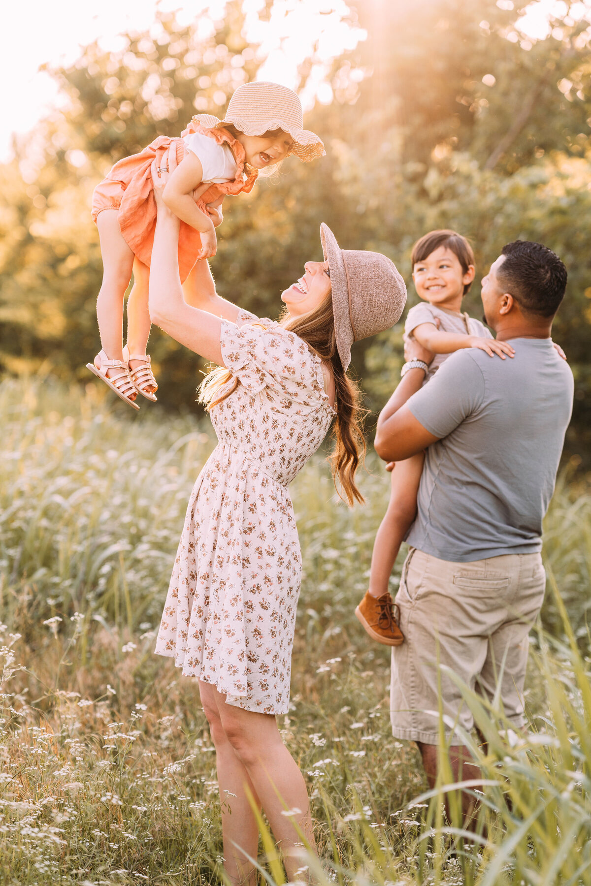 father holds son while mother holds daughter in the air in wildflower field
