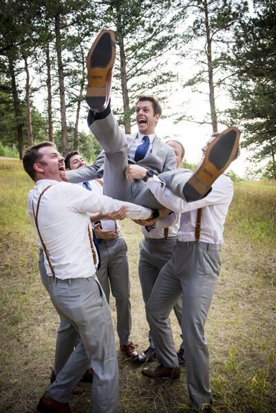 A groom is thrown into the air by his groomsmen as they all laugh.