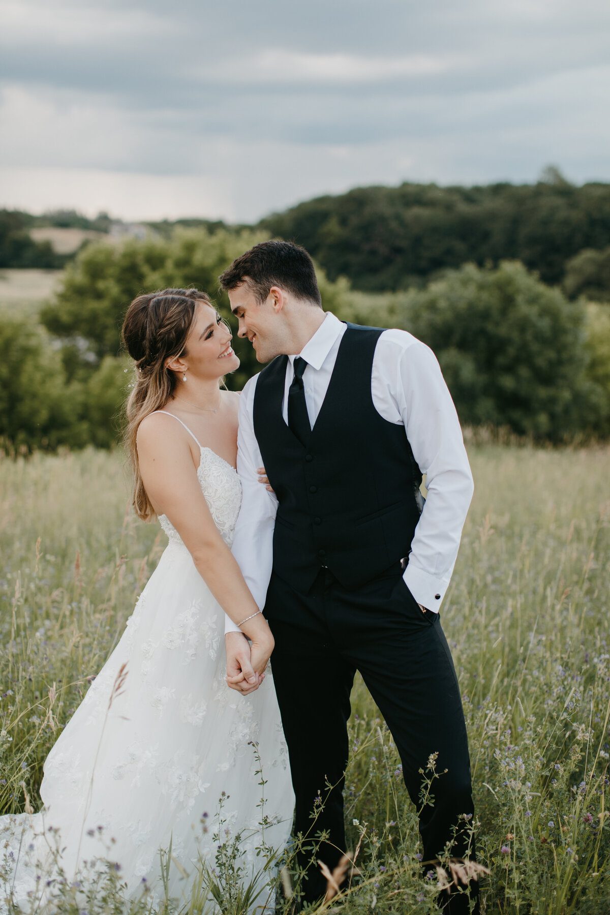 Bride and groom holding hands and smiling at each other in a grassy field