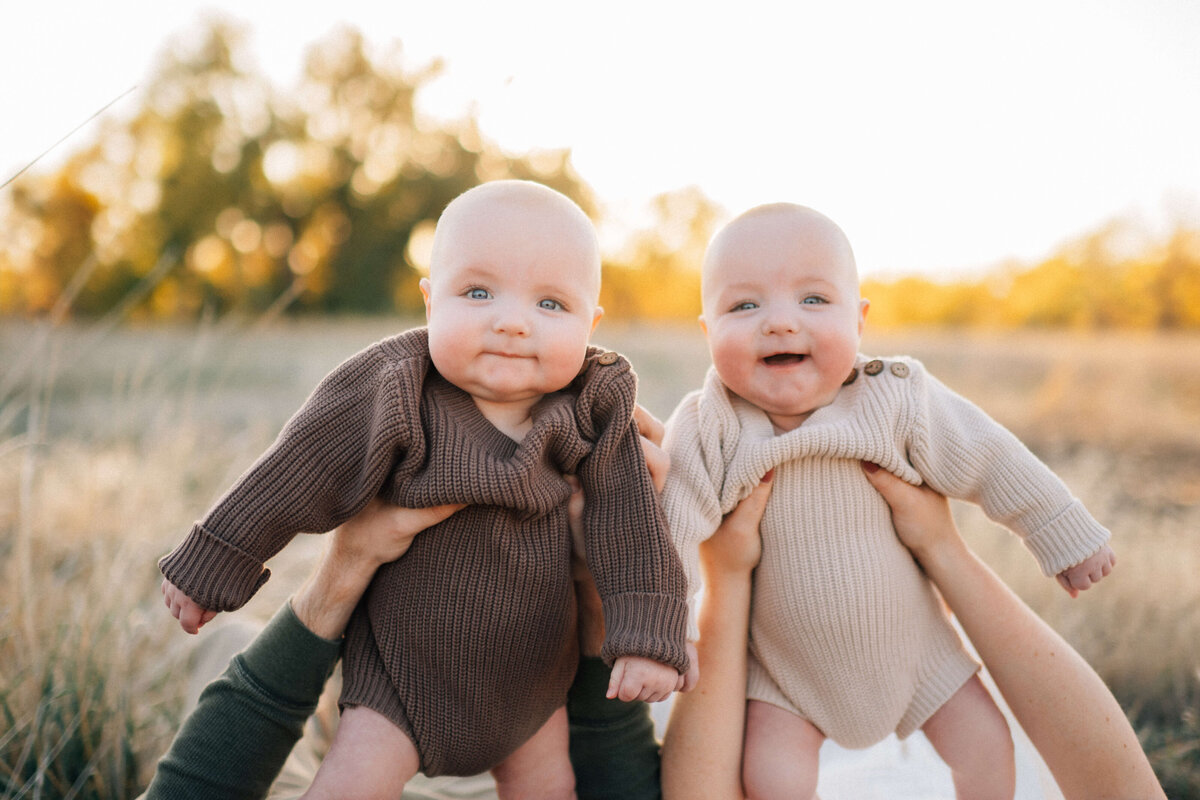 twin baby boys being held up by their parents while they smile at the photographer
