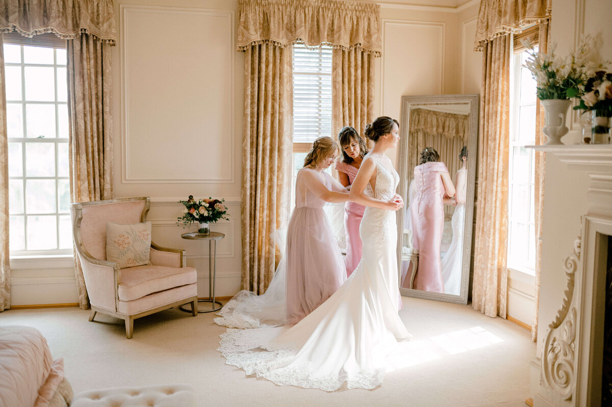 Mother of bride helping bride zip her dress for getting ready photos