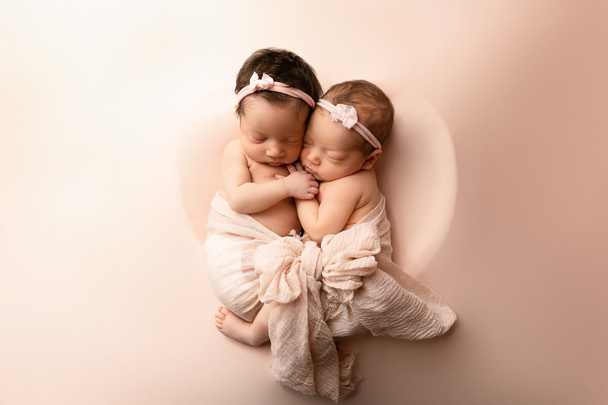 Baby girls posed together in a heart shape during their newborn photo session.