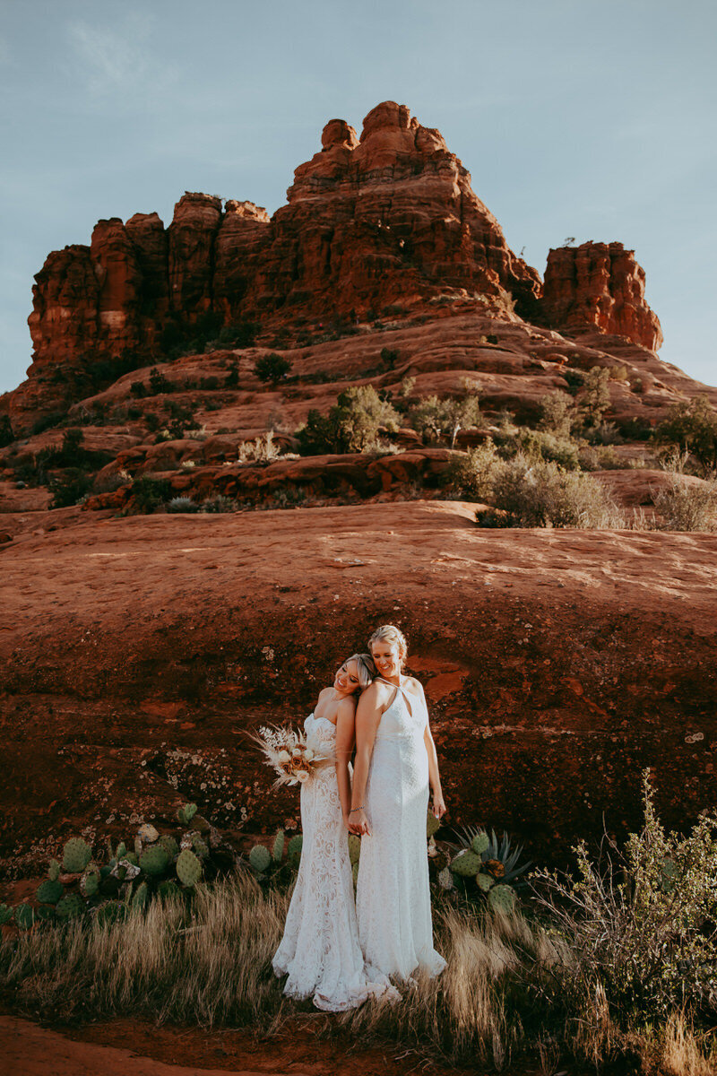 two brides stand hand in hand in front of red rocks