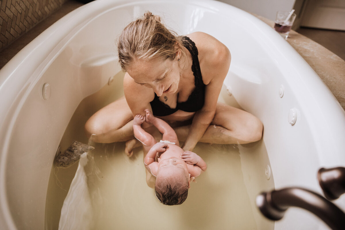 woman in herb bath holding looking at her newborn