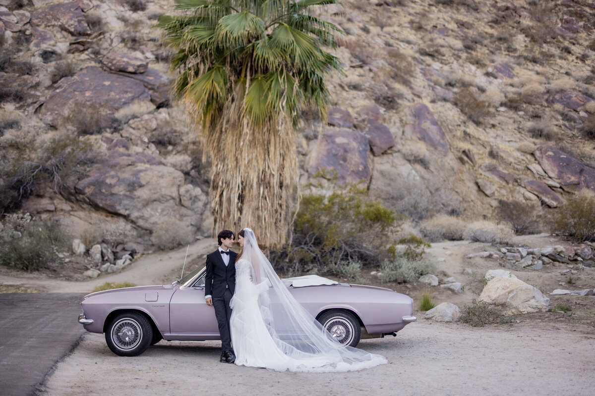 Couple posing beside classic convertible with rocky Palm Springs backdrop.