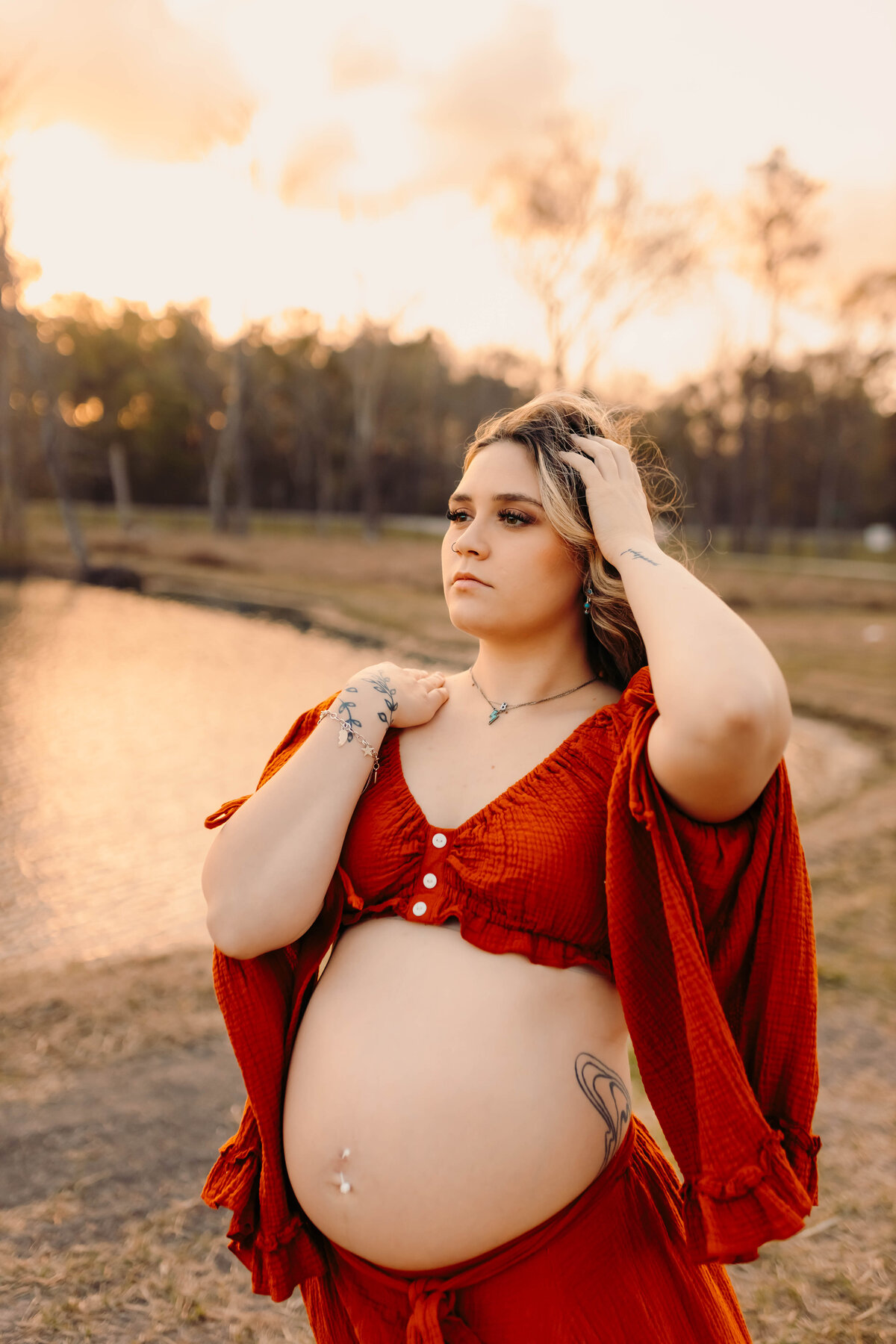 Kingwood TX maternity photography – expecting mother in burnt orange gown holding baby bump, outdoor golden-hour portrait
