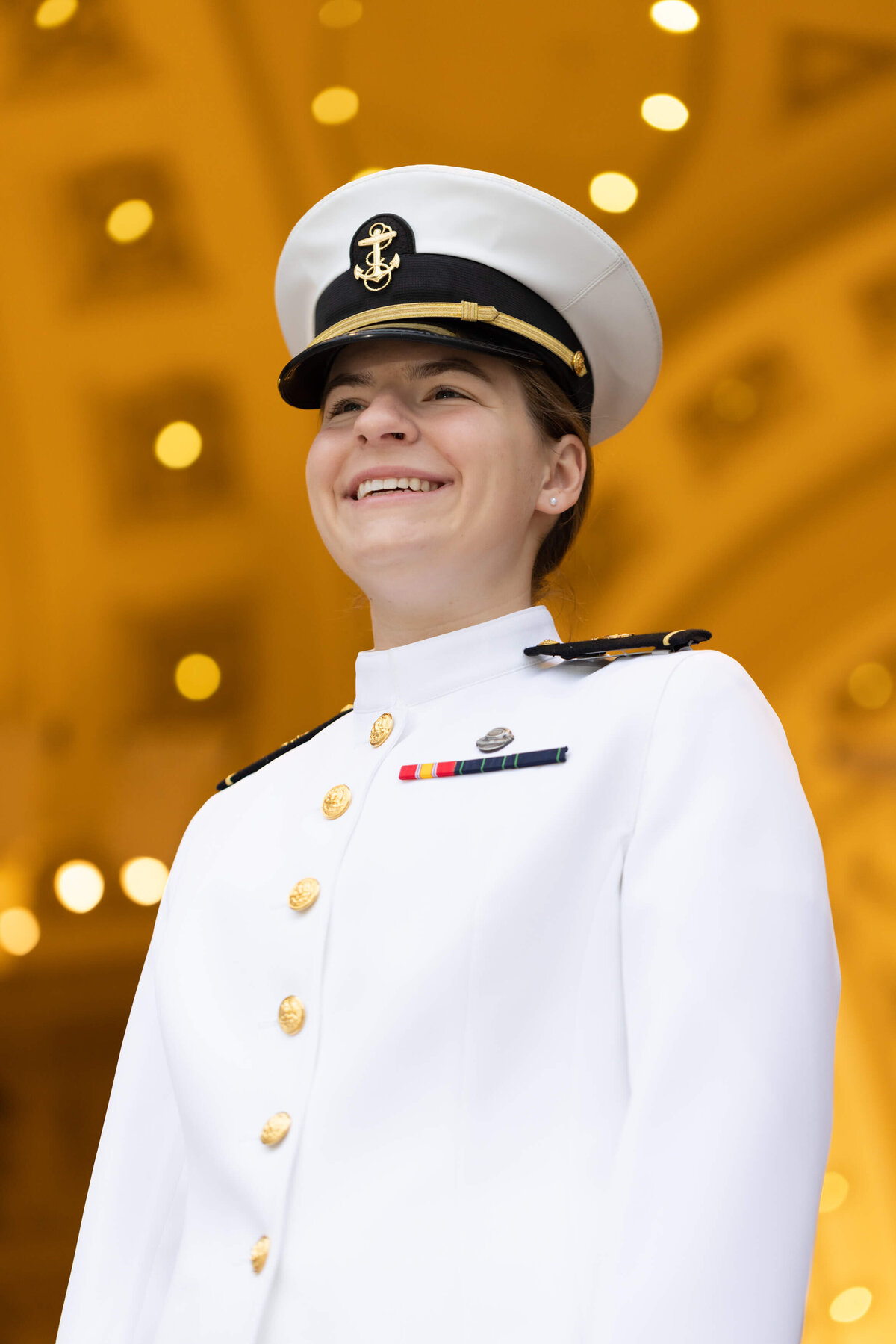 Naval Academy graduate woman smiles in a white uniform with Bancroft Hall Rotunda in the background.