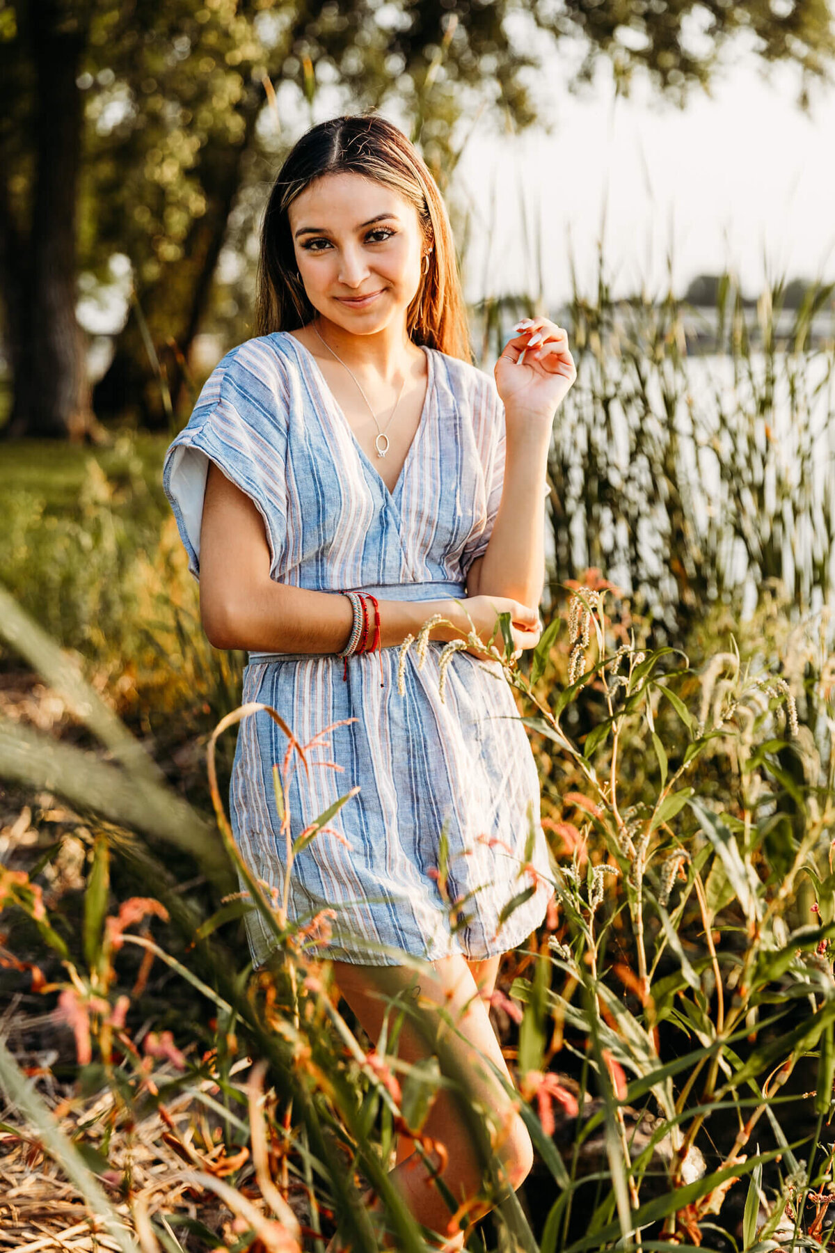 senior resting her elbow in her hand while standing in cattails for senior photo session