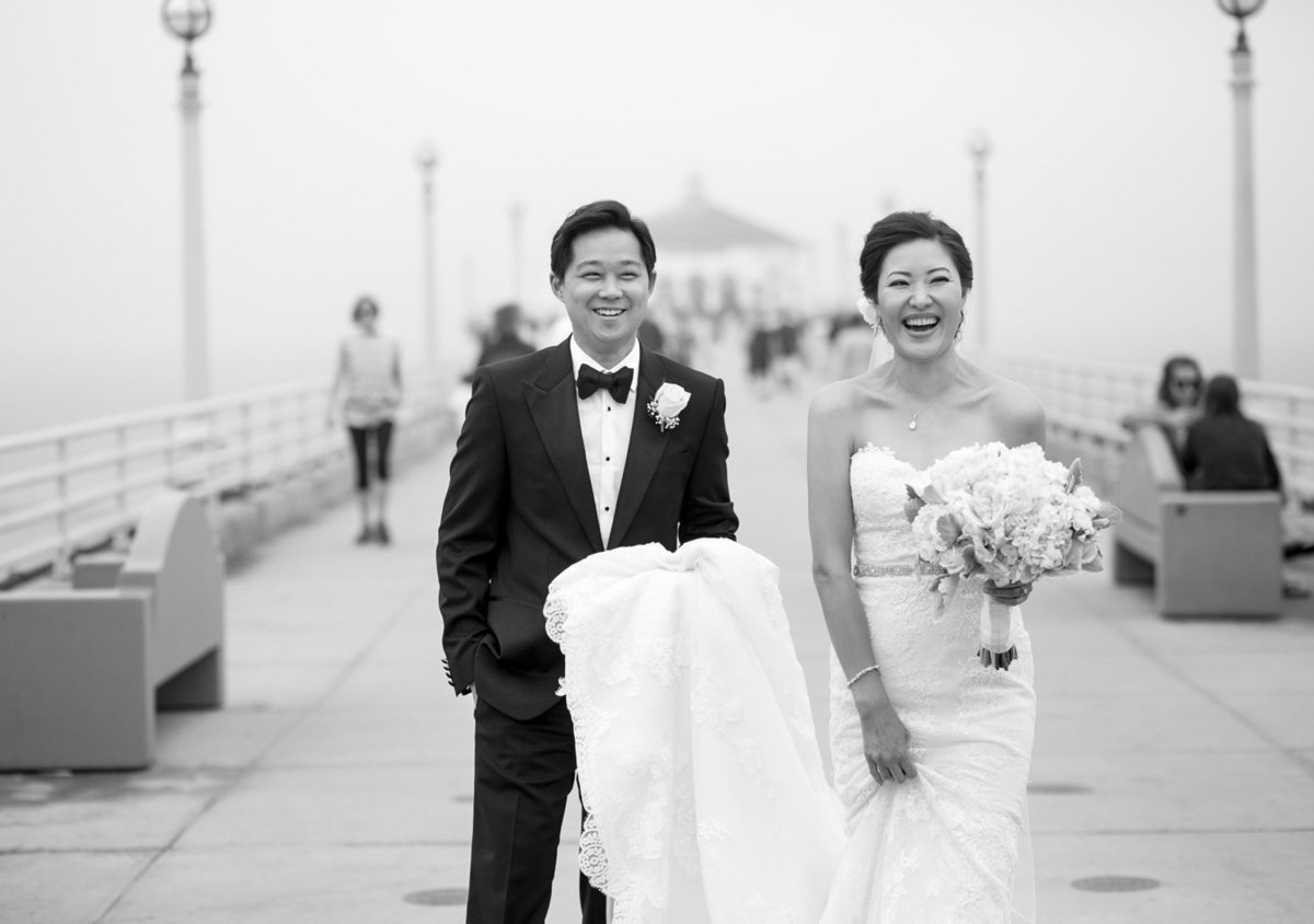 Groom holding his bride's wedding dress train on Manhattan Beach pier