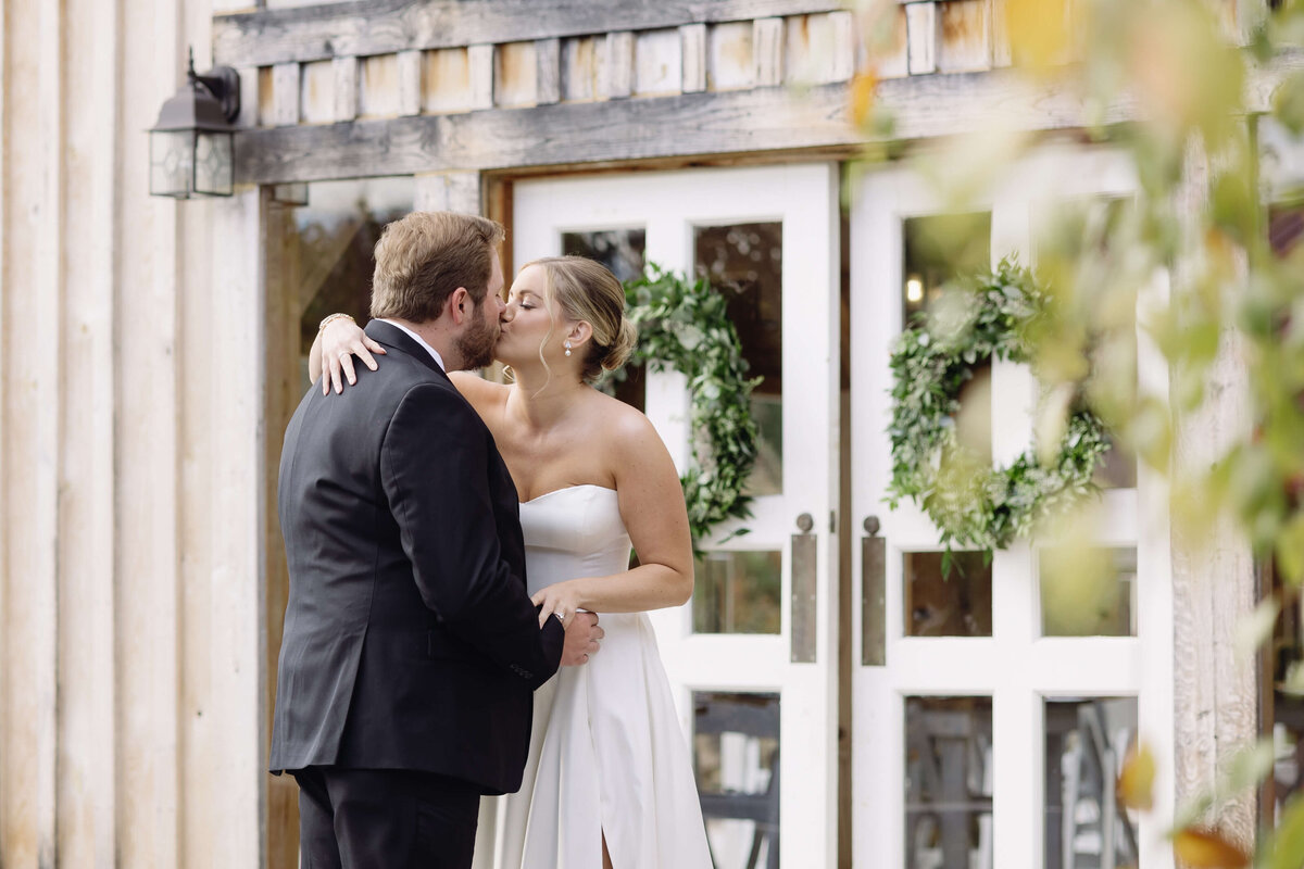 bride and groom kissing each other outside of their wedding venue with brides arm around the grooms shoulder photographed by Virginia wedding photographer
