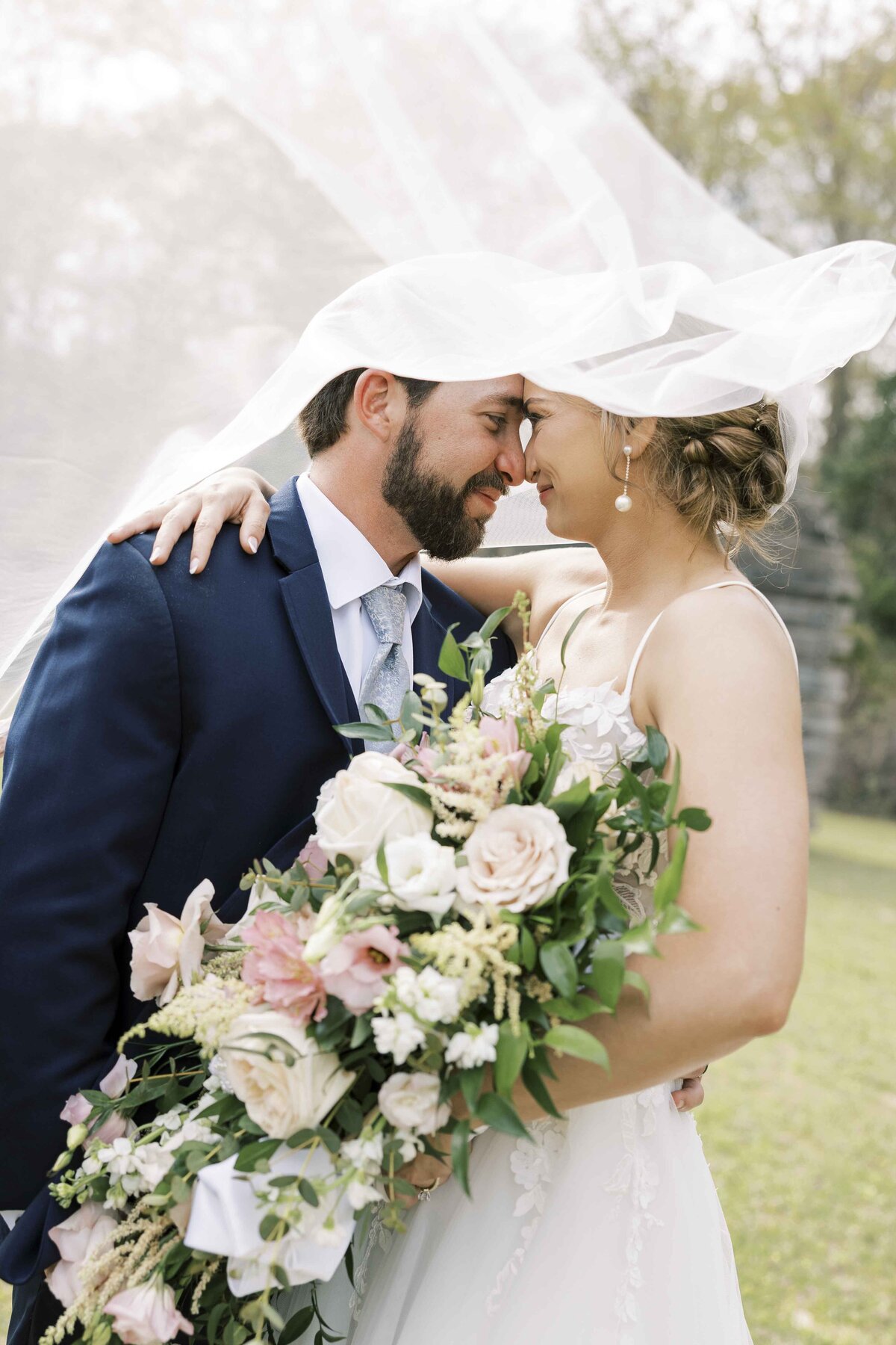 bride and groom touching noses while wrapped in bride's veil