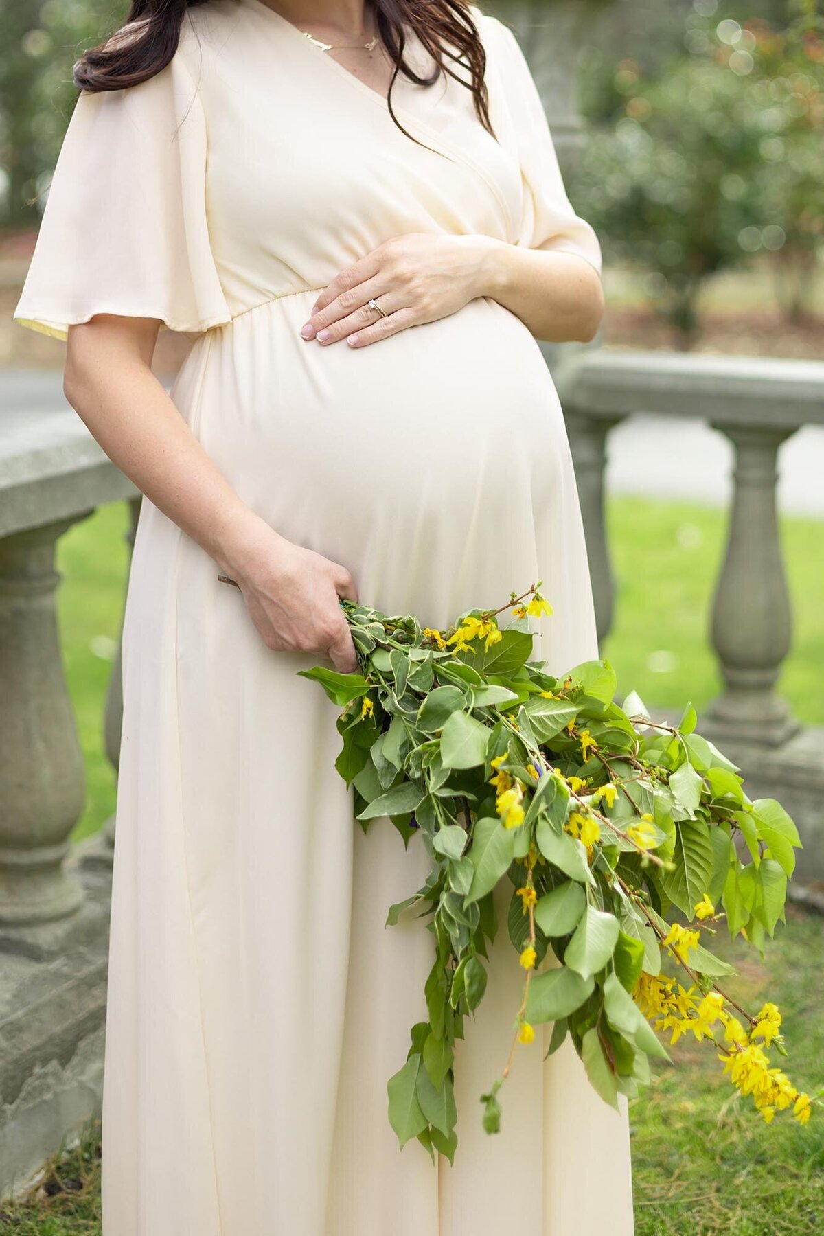 Photo of a Woman with a loose bouquet of greenery and florals while touching the top of her belly  by Virginia Beach Maternity Photographer Mary Eleanor Photography