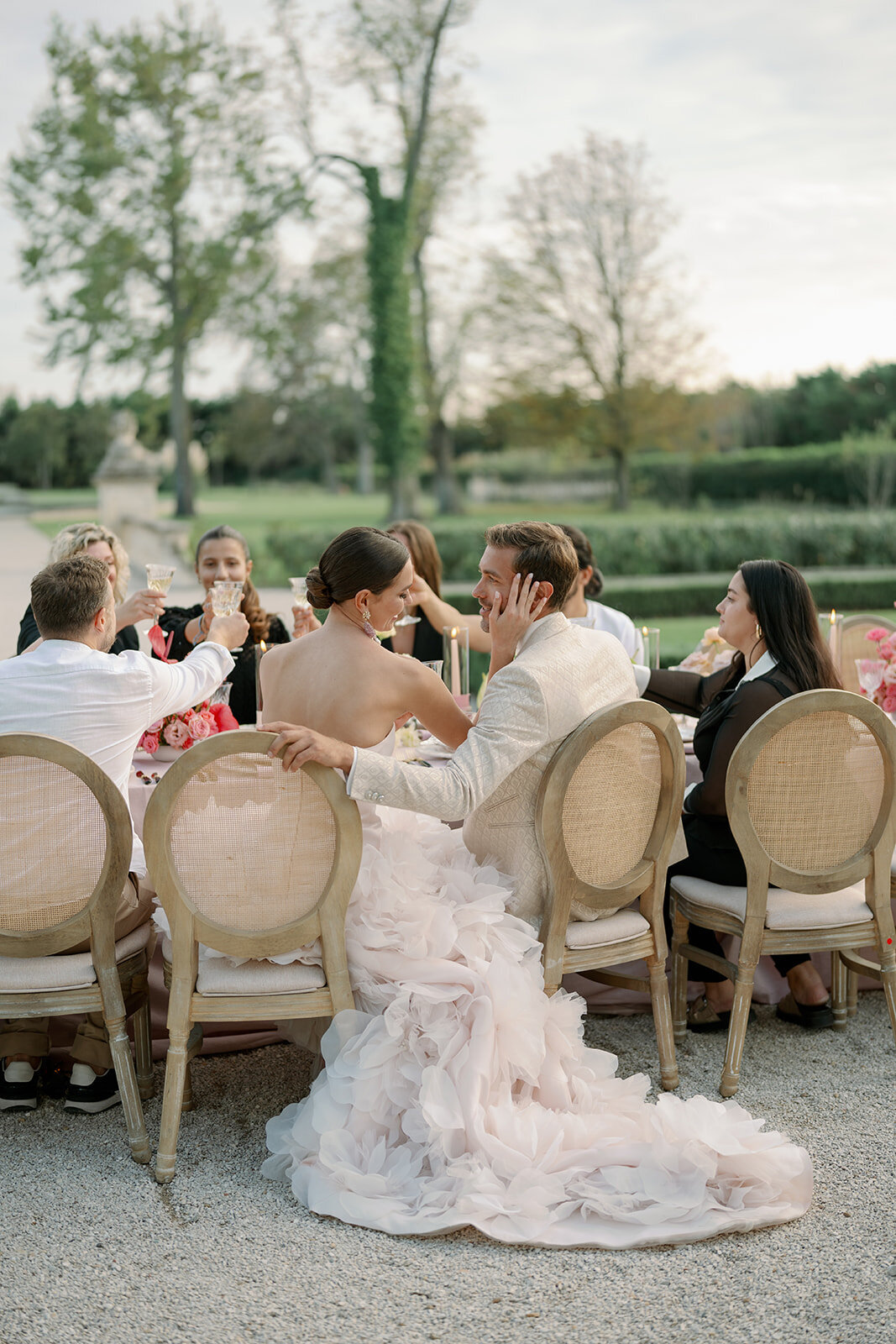 Bride and groom enjoying dinner with guests during outdoor wedding reception overlooking gardens at Château de Tourreau.
