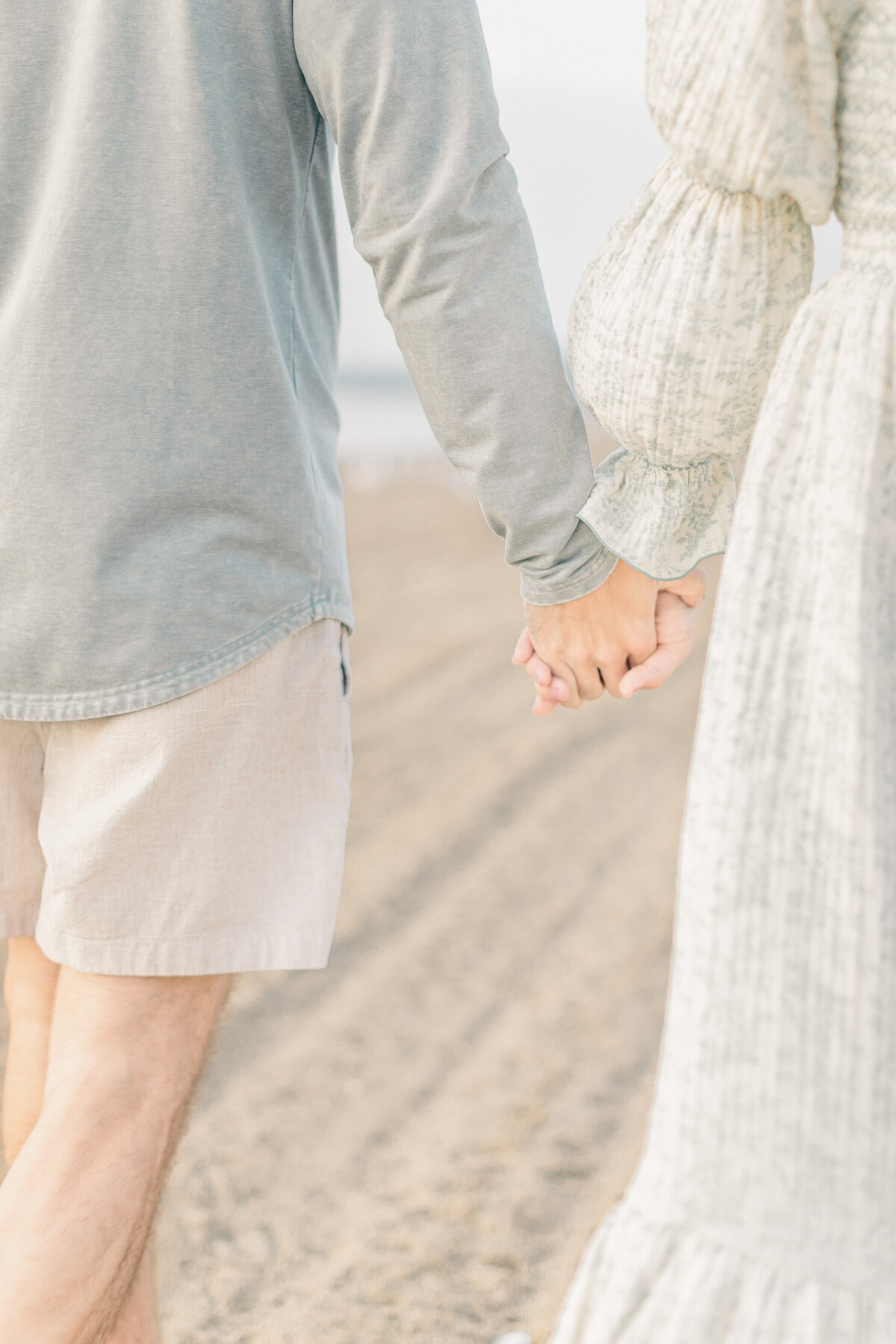 Close-up of parents walking hand in hand on the sand during their Kansas City lake session with their baby boy held safely in their arms. 