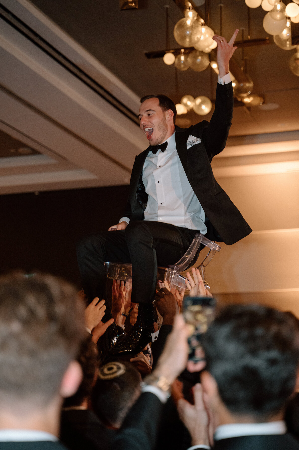 Groom lifted up in a chair celebrating joyfully during the hora dance at a lively Toronto wedding reception.