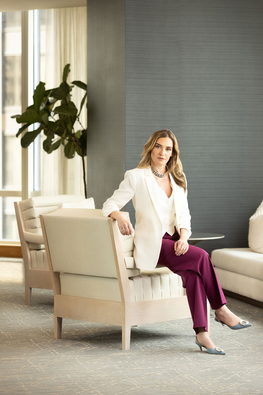 Woman in white blazer and burgundy pants sitting on a chair