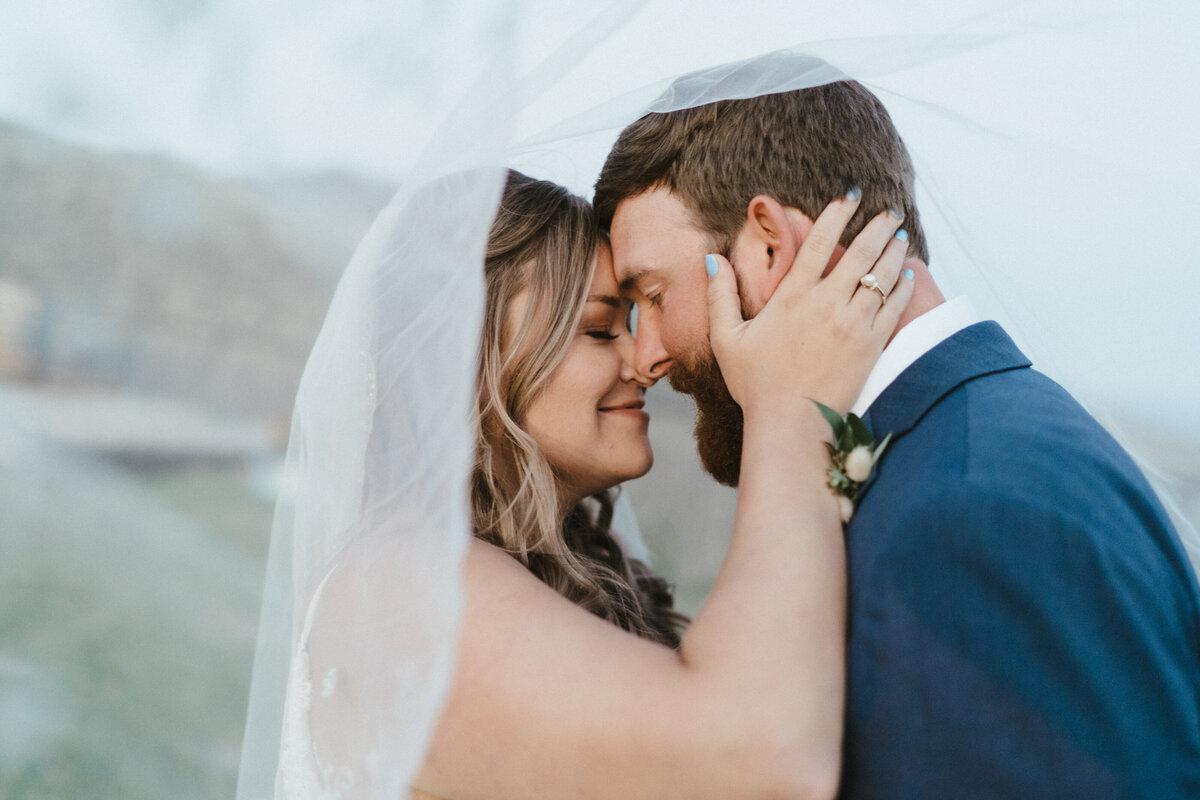 Bride and groom pose under the bride's veil on their wedding day.