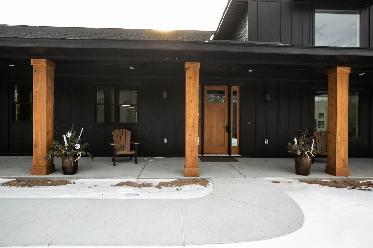 Exterior view of custom home in Elk River, Minnesota with black siding, wood details and front porch built by Cornerstone Custom Builds