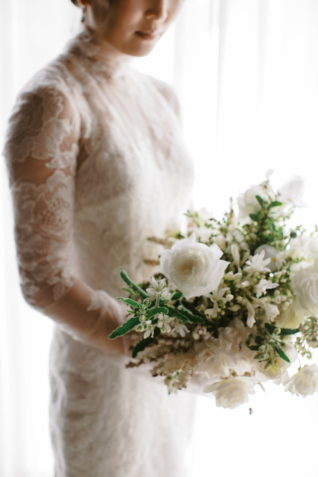 bride holds white bouquet wearing long sleeve lace wedding dress