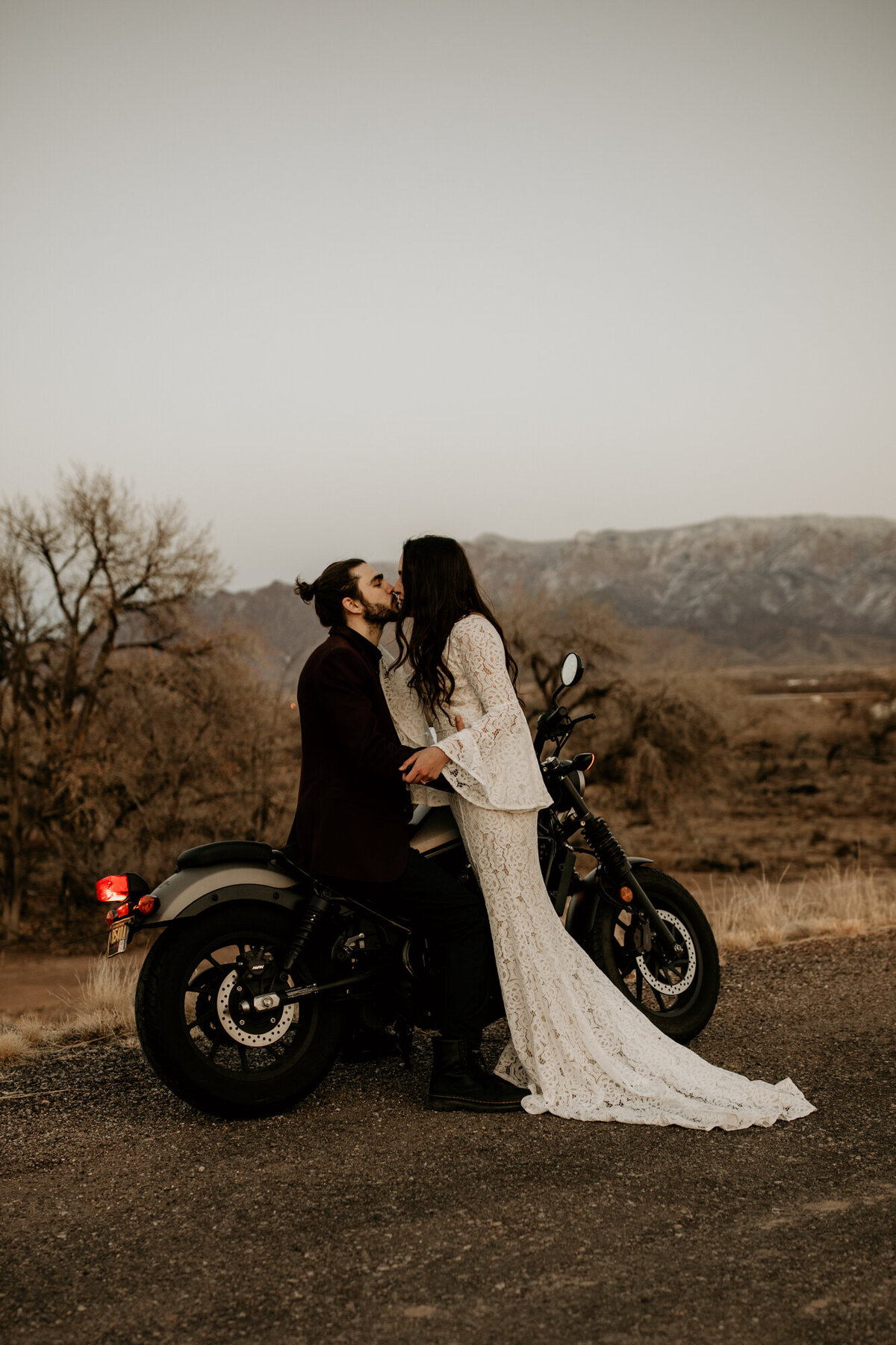 groom sitting on motorcycle in the desert kissing bride