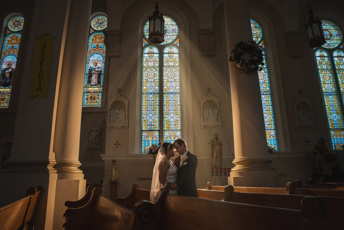 Wedding couple by stained glass window.