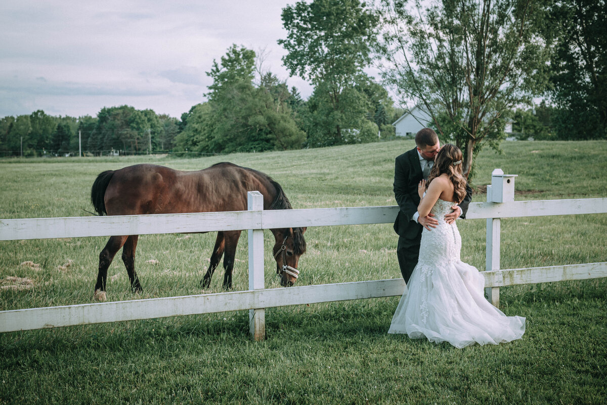 Couple kiss by white fence and horses